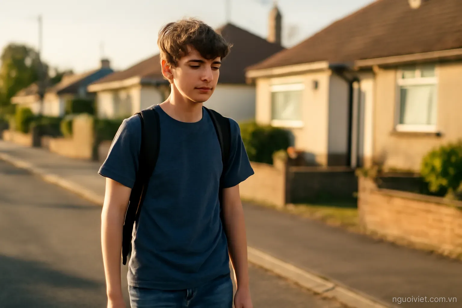a teenager walking home past low houses in late afternoon with a backpack on one shoulder