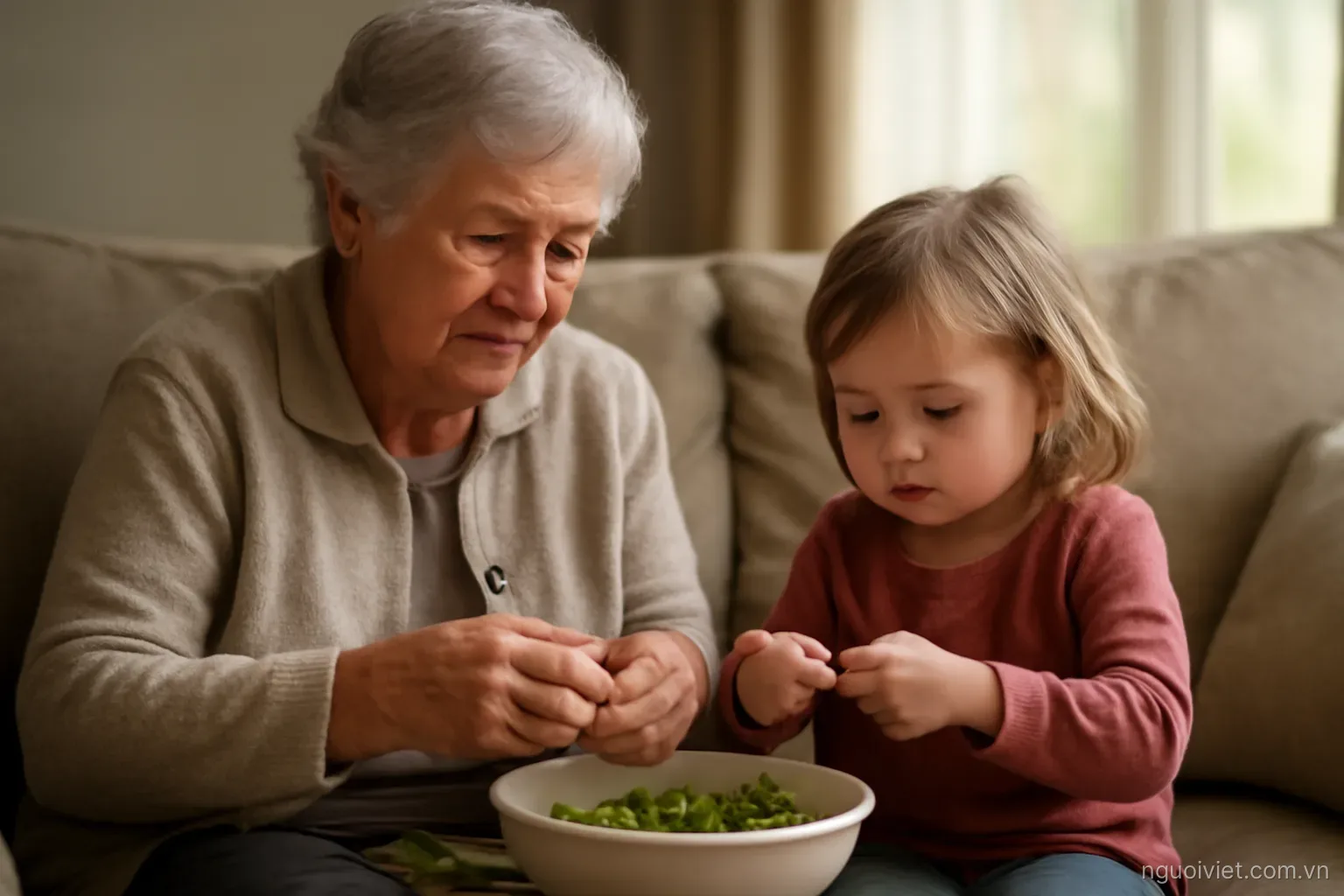 an elderly woman and a small child sitting together on a sofa shelling beans into a bowl